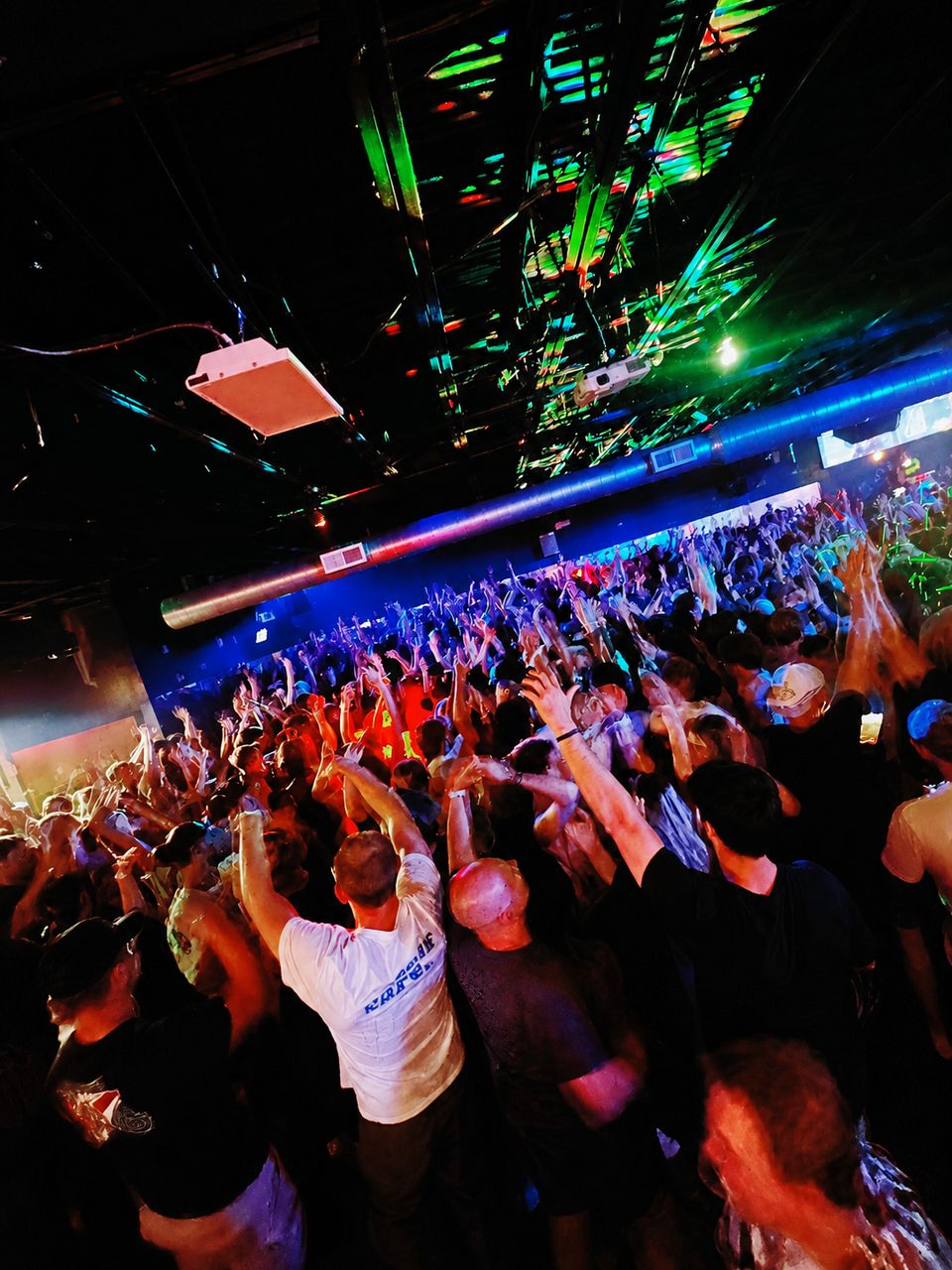 A packed crowd on the floor at The Woods under blue and red stage light, hands in the air.