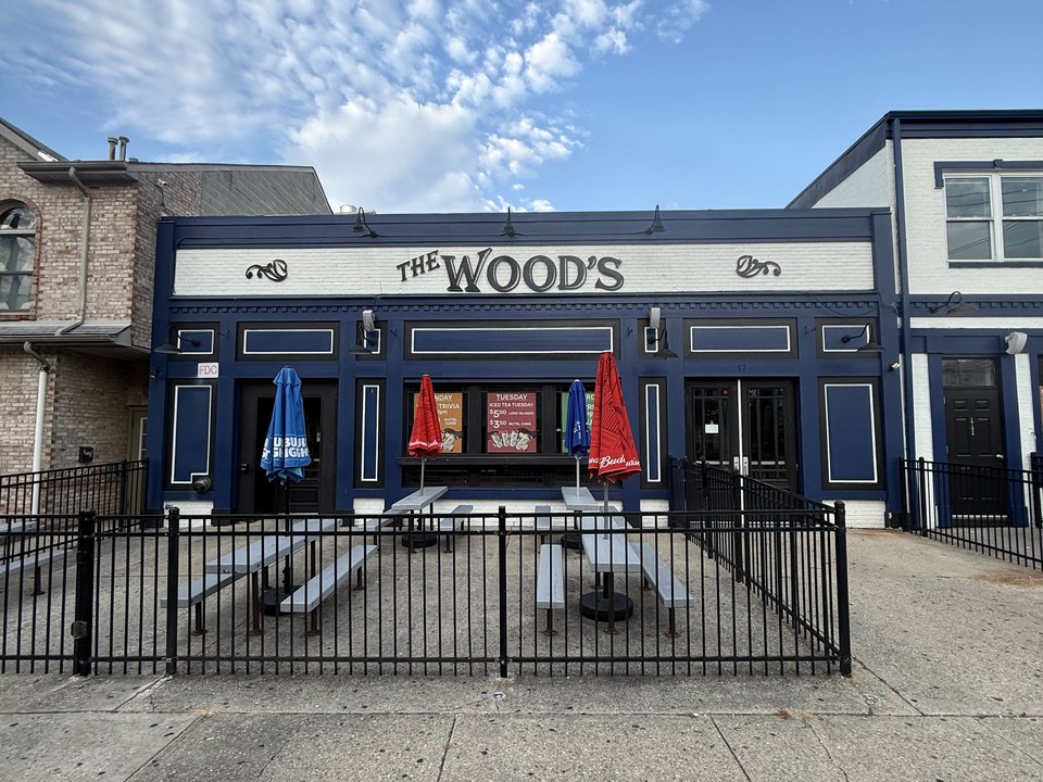 The Wood's storefront in daylight: a navy façade with the name on a white sign band, and picnic tables behind a rail out front.